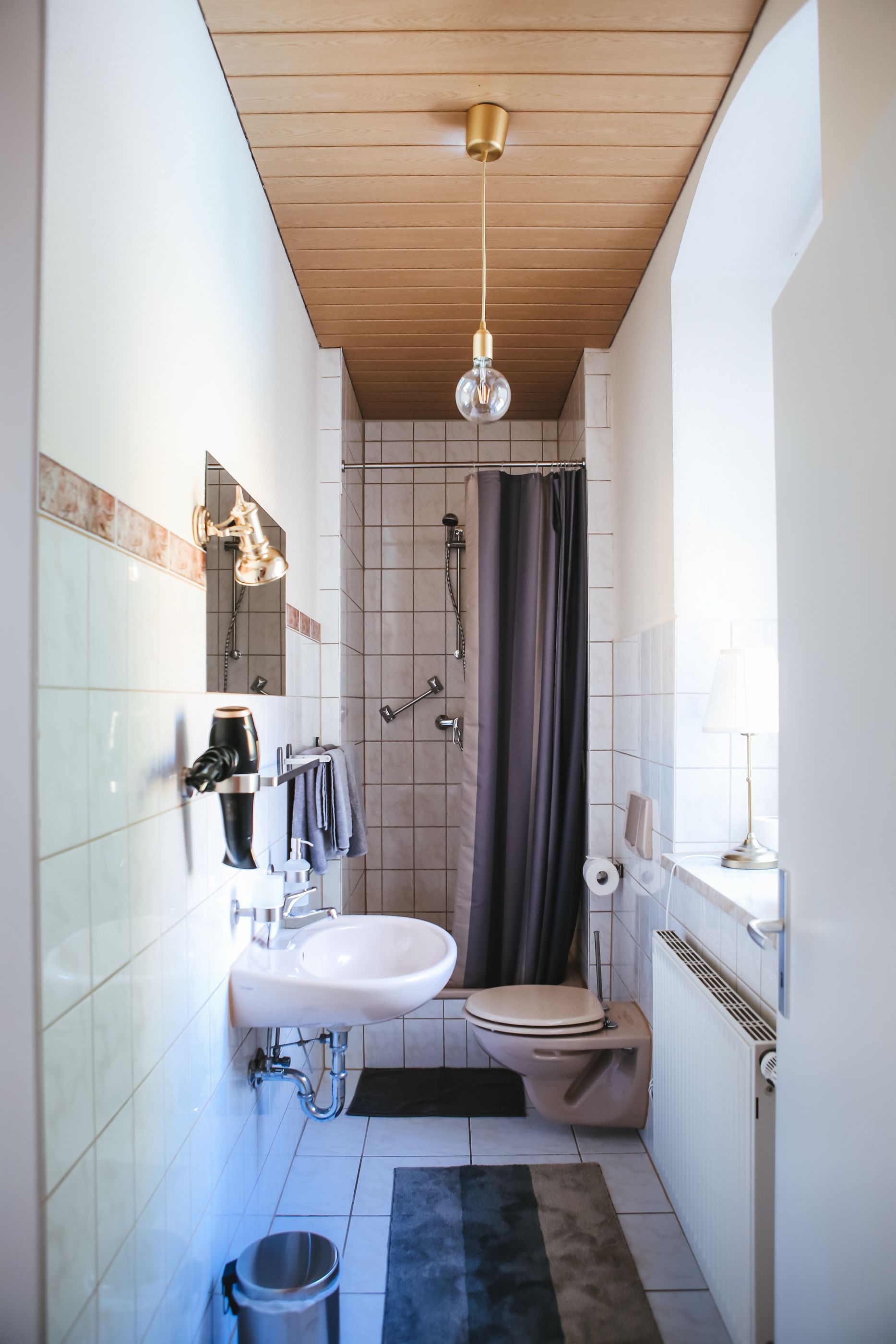 Ein kleines Badezimmer mit Waschbecken, Toilette, Dusche und einer Deckenleuchte.