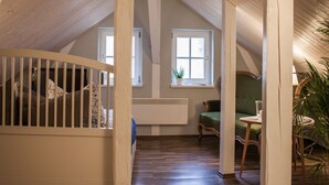 A spacious attic room with wooden beams, a staircase, a green sofa, and a small table. - ApartOne (Bautzen)