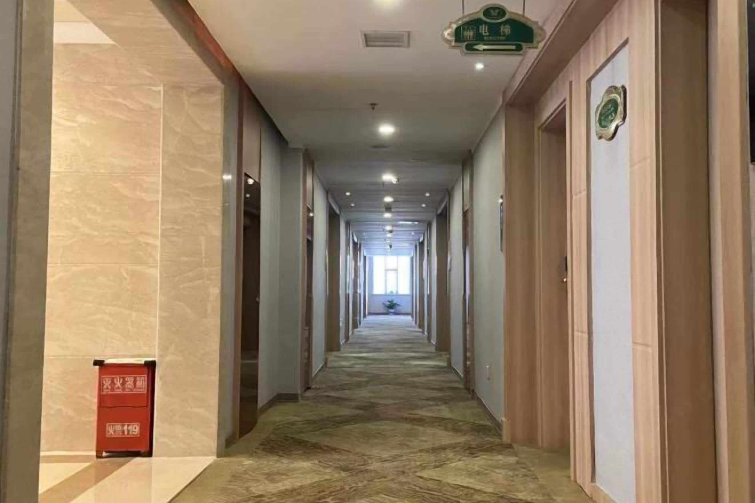 Pasillo de hotel con piso alfombrado, puertas a ambos lados y un basurero a la izquierda.