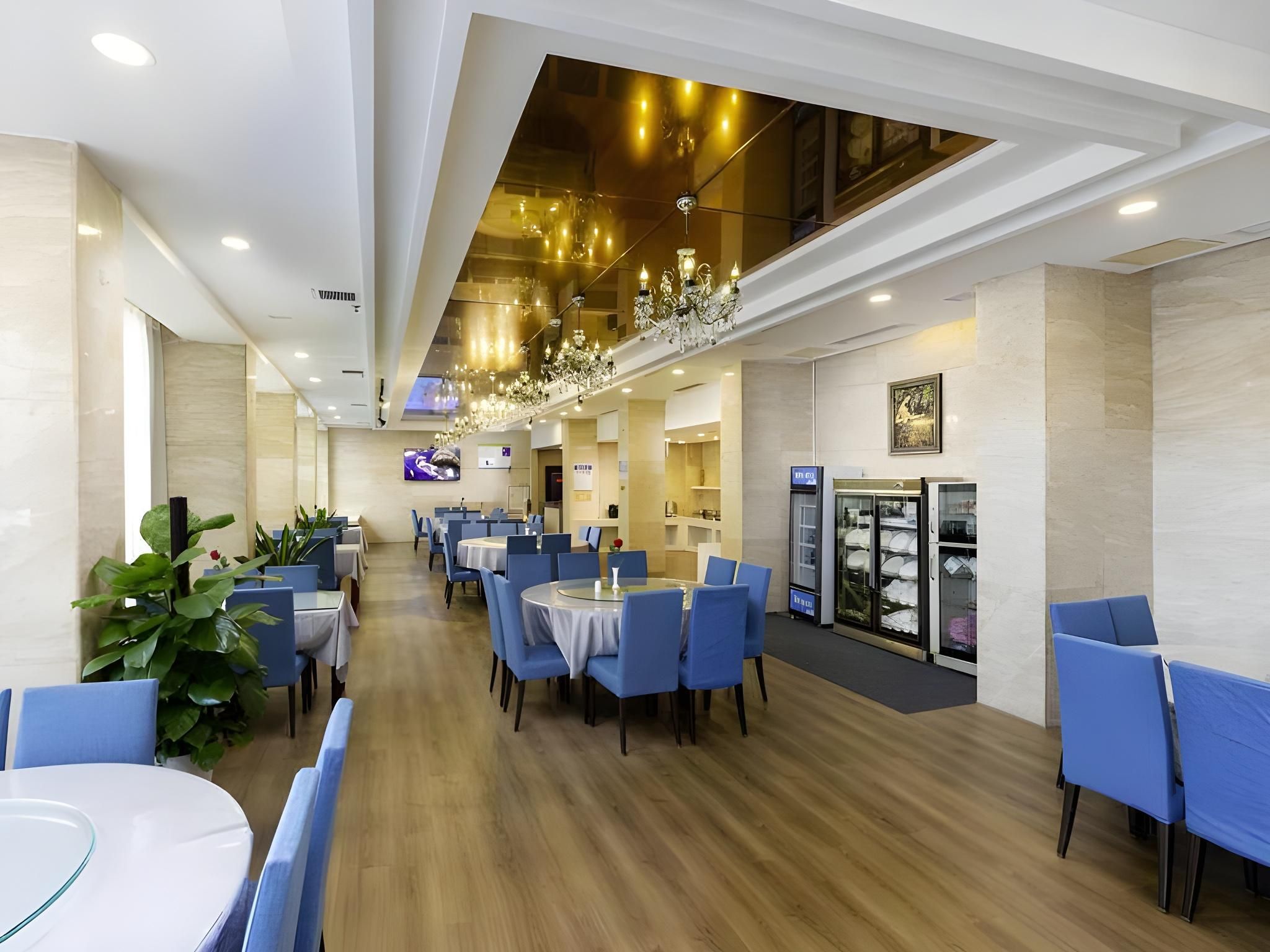 A modern dining area with round tables and blue chairs, a chandelier, and a glass display case with plates.