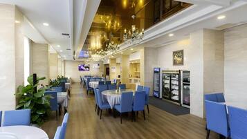 A modern dining area with round tables and blue chairs, a chandelier, and a glass display case with plates.