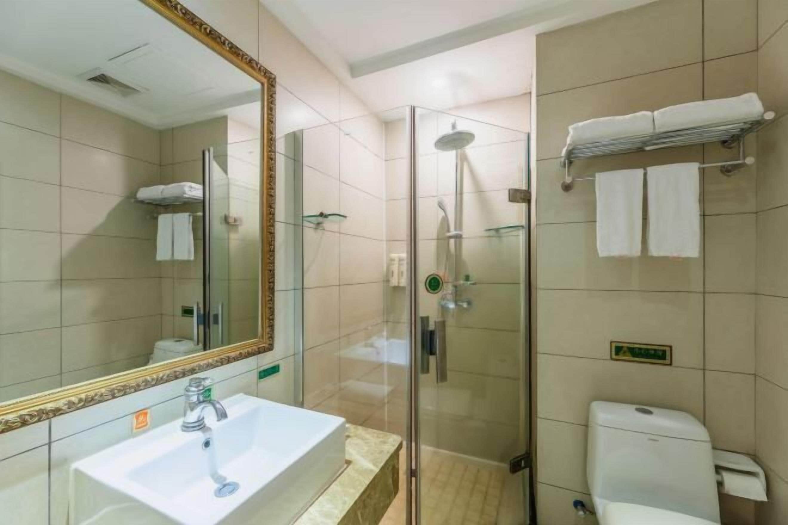 Une salle de bain moderne avec une douche à parois de verre, un lavabo blanc et un grand miroir doté d’un cadre décoratif.