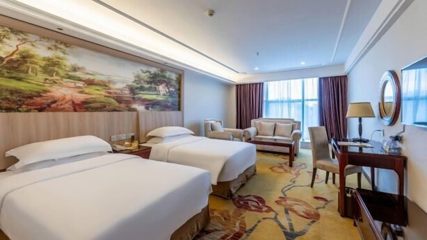 A hotel room with two beds, a desk, a chair, a large painting, and a view of the outdoors. - Vienna Classic Hotel (Shangrao Pedestrian street Peace Sunshine) (Shangrao)