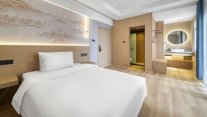 A hotel room with a large bed, a wall-mounted artwork, a bathroom with a mirror, and a wooden floor.