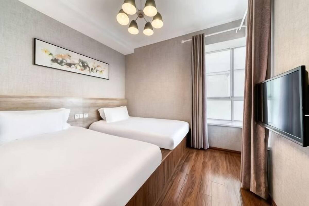 A hotel room with two beds, a flat-screen TV, a painting on the wall, and a large window.