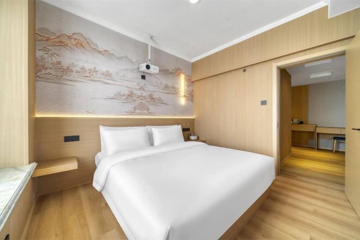 A modern bedroom with a large bed, a wall-mounted projector, and a wooden floor.