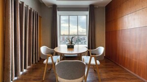 A modern dining area with a round table and four chairs, a city view through large windows, and wooden paneling on the walls.