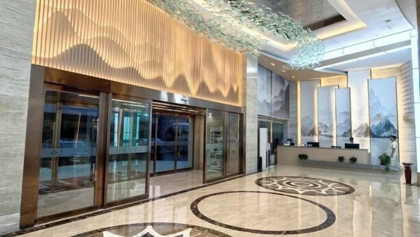A modern lobby with a glass entrance, a patterned floor, and a reception desk with a mountain mural.