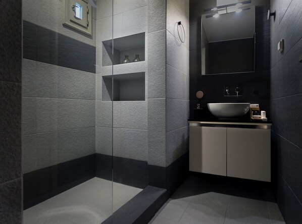 Une salle de bain moderne avec un grand lavabo, des carreaux foncés et des étagères intégrées.