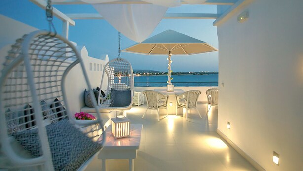 Una terraza al aire libre con mobiliario de mimbre blanco, una silla colgante y una mesa con lámpara.