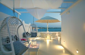 Une terrasse extérieure avec des meubles en osier blanc, un fauteuil suspendu et une table avec une lampe.