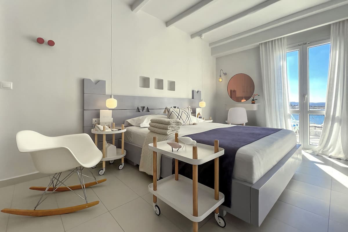 Una habitación de hotel moderna con una cama grande, un escritorio, un sillón mecedora y vistas al mar.