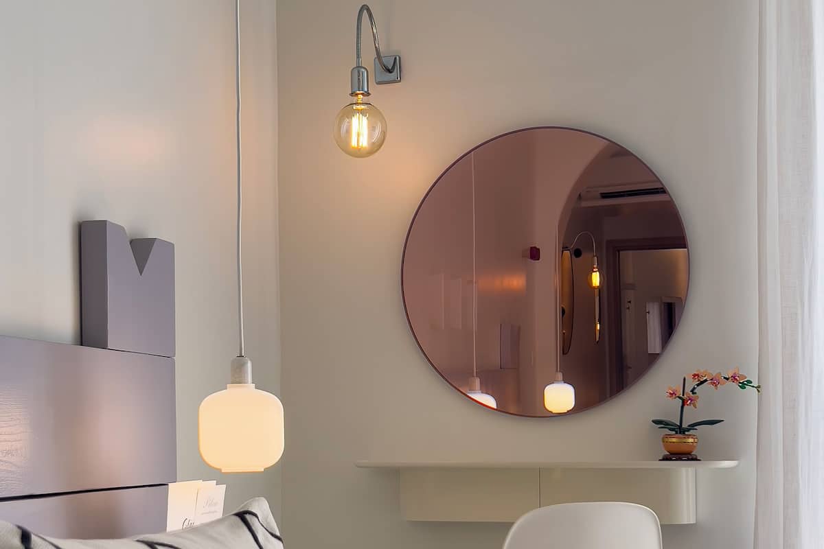Una habitación de hotel moderna con una cama, un espejo redondo, una silla blanca y una mesita.