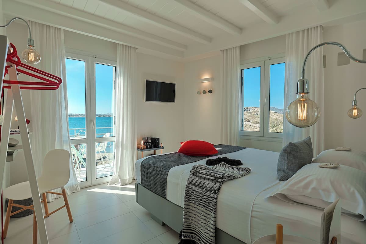 Un dormitorio moderno con cama, mesitas de noche, televisor y vistas al mar.