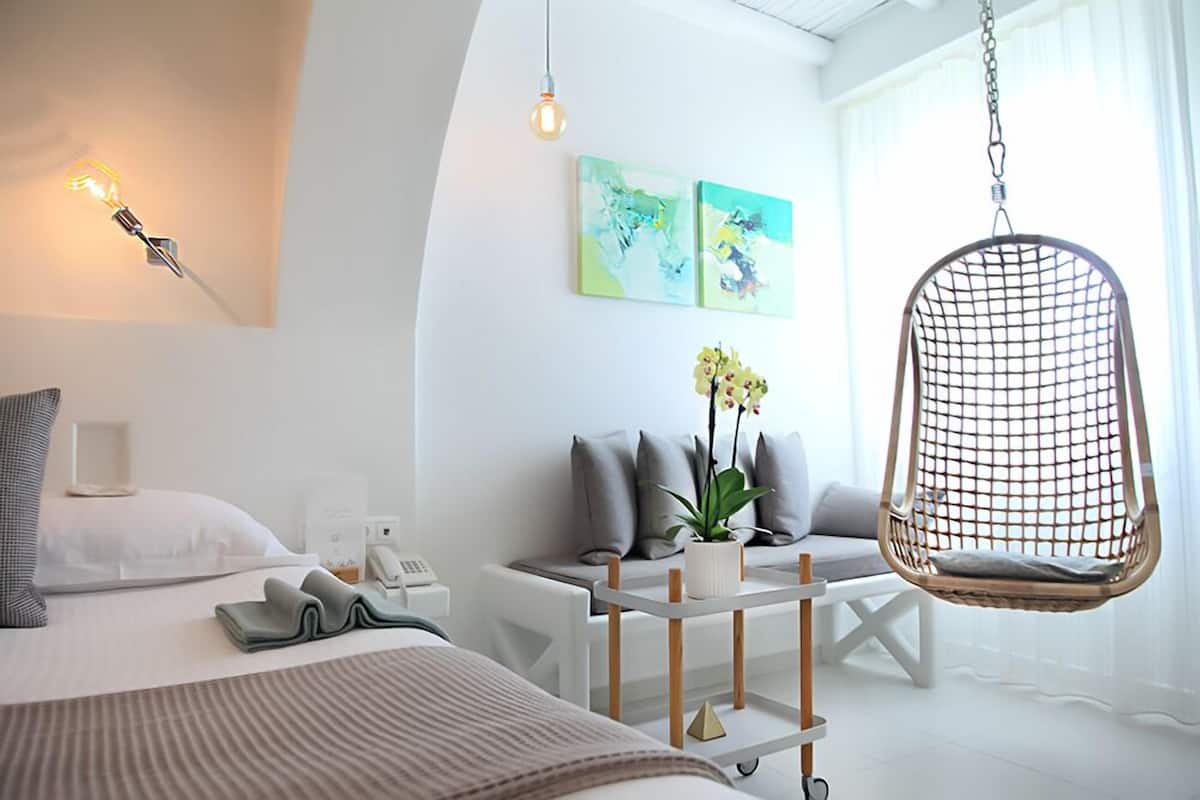 Habitación de hotel moderna con una cama, una silla colgante, una mesita con una planta y obras de arte en la pared.