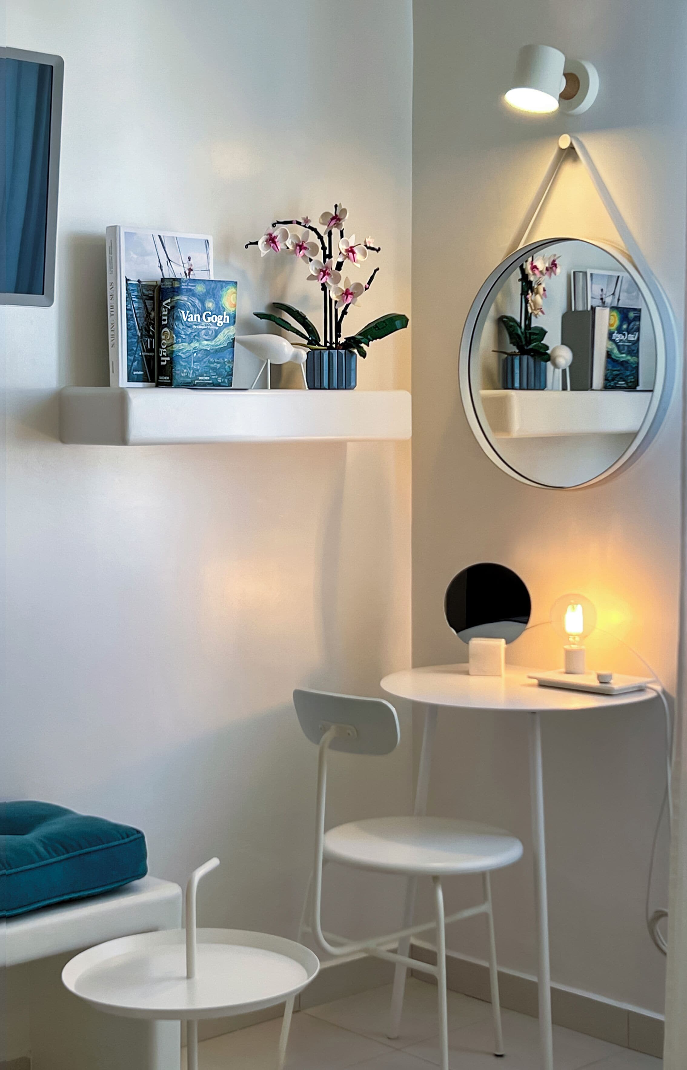 Une chambre moderne avec des meubles blancs, un miroir rond et des étagères ornées de livres et de fleurs.