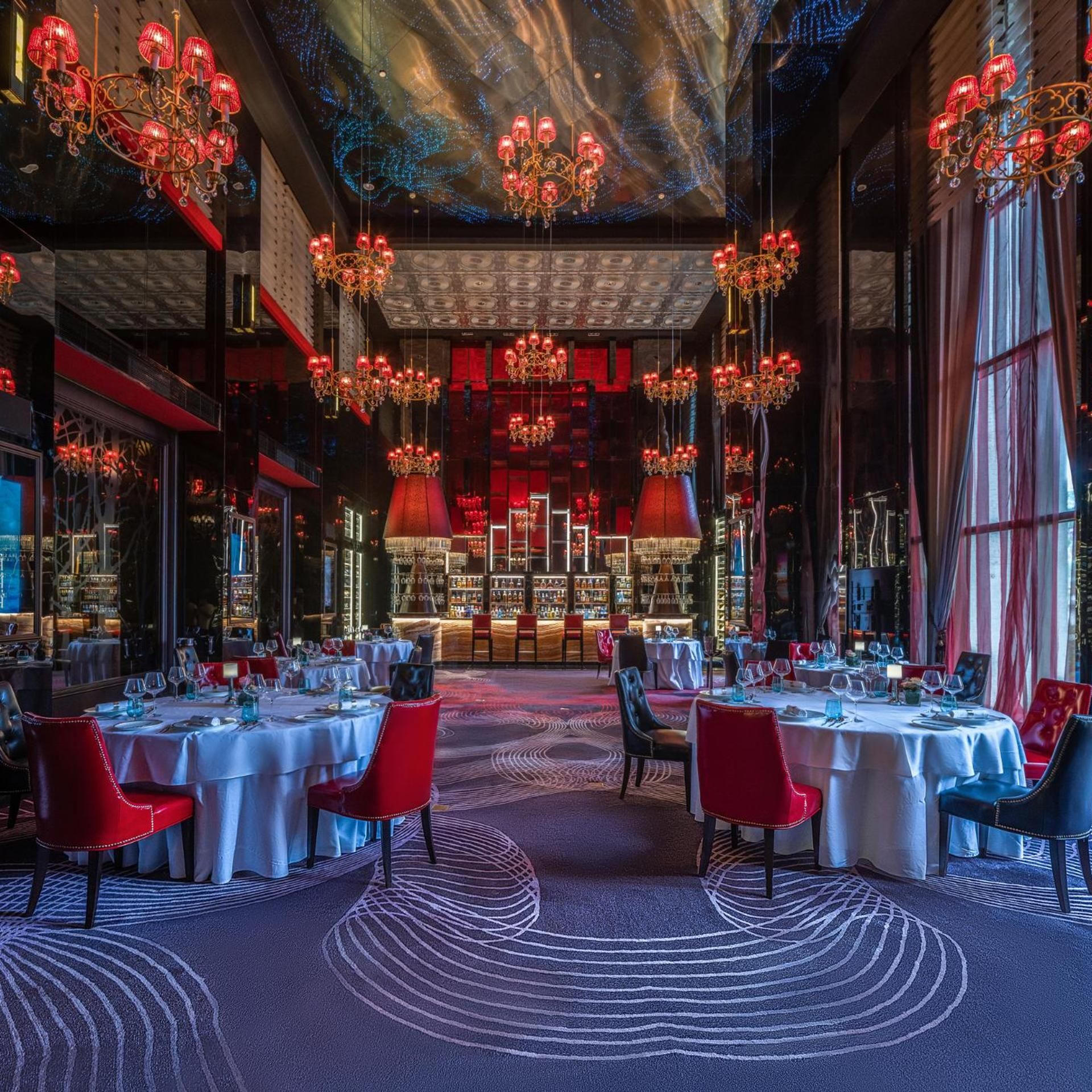 Un restaurant avec des tables rondes, des chaises rouges et des lustres.