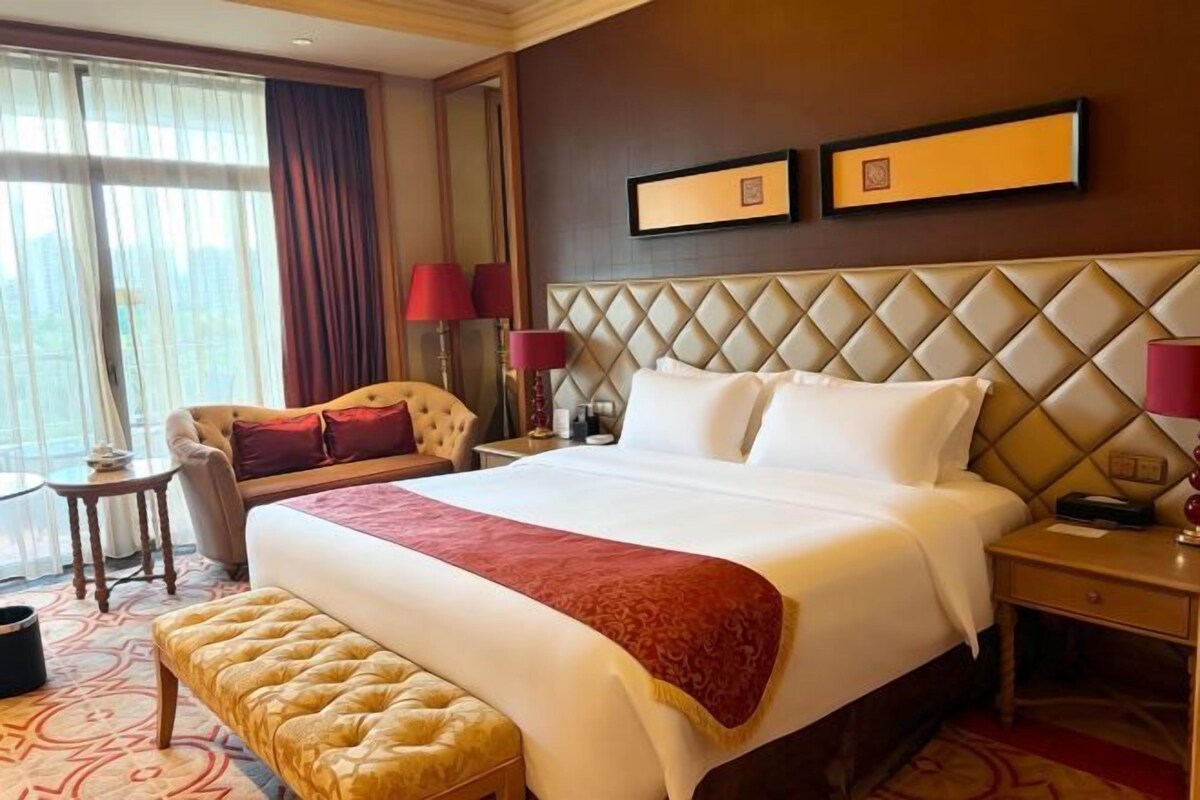 A hotel room with a large bed, a sitting area with a chair, a small table, and a bench.