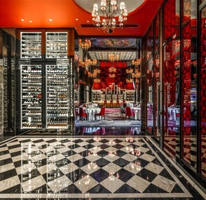 A hotel lobby with a checkered floor, wine racks, a dining area, and a chandelier.