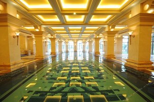 Una amplia piscina interior con un diseño geométrico de azulejos, rodeada de columnas e iluminación empotrada.