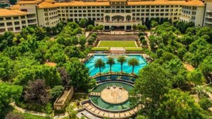 A hotel with a central pool, surrounded by lush greenery and a city skyline in the background. - Jinjiang International Hotel Ganzhou (GANZHOU)