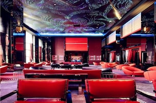 Vestíbulo de hotel con asientos rojos, una pantalla digital en el techo y una zona de bar.