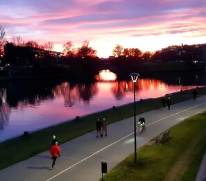 A riverside path with people walking and cycling, a lamp post, and a bench.