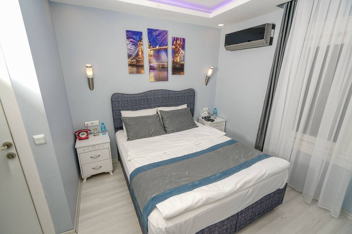 A bedroom with a bed, bedside tables, a nightstand, a wall-mounted TV, and artwork depicting a cityscape.