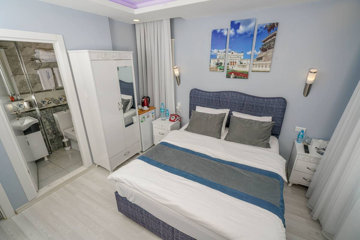 A modern hotel room with a large bed, a wardrobe, a vanity with a mirror, and a bathroom visible through an open door.