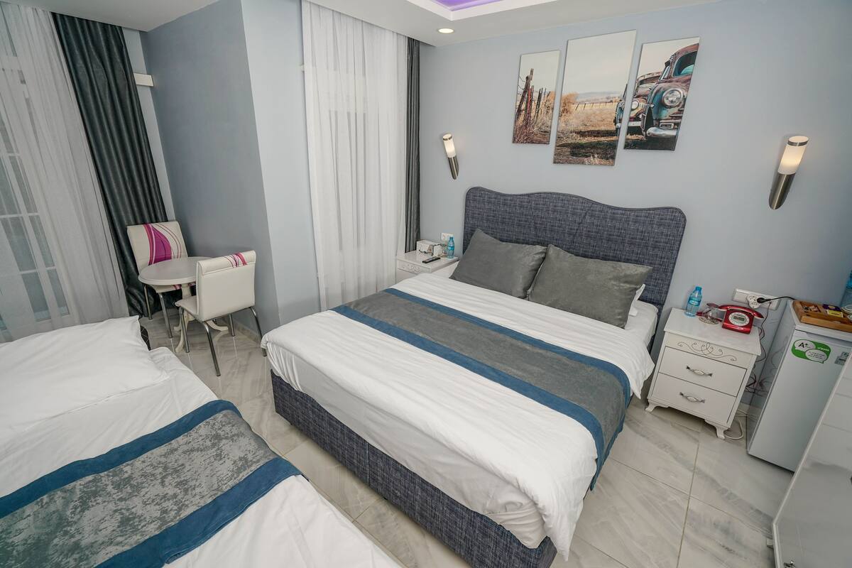 A hotel room with a large bed, a desk, a chair, and a small refrigerator.