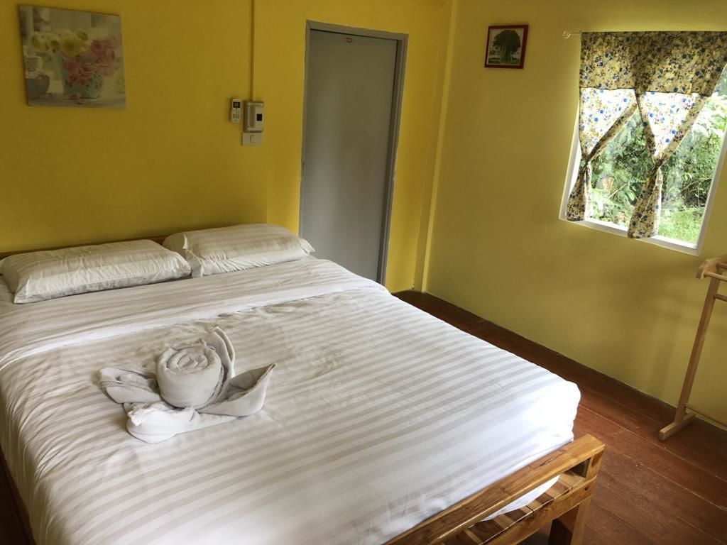 A hotel room with a bed, a door, a window with a view, and a wall-mounted phone.