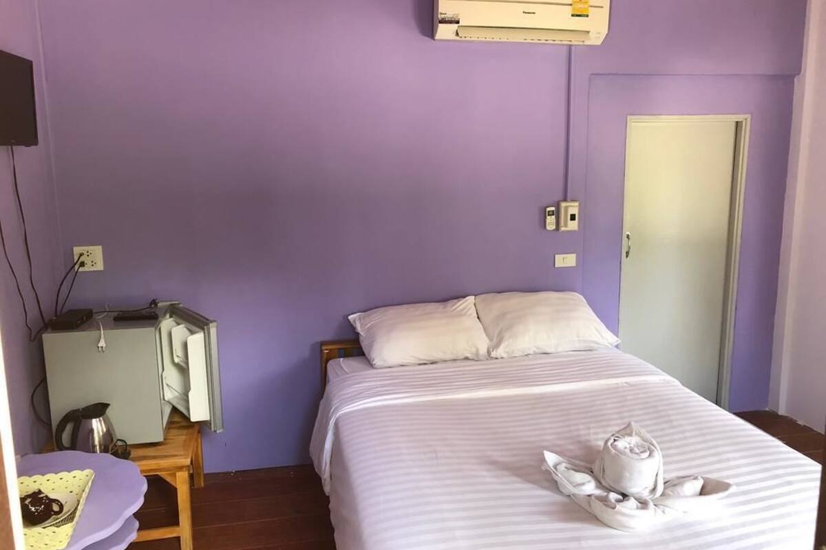 A room with a bed, a desk with a kettle, and an air conditioner on the wall.