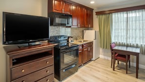 A compact kitchen with wooden cabinets, a microwave, stove, and a flat-screen TV. - Quality Inn & Suites El Cajon San Diego East (El Cajon)