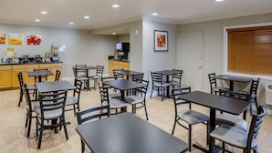 A hotel dining area with multiple tables and chairs, a kitchen area with a coffee machine, and a clock on the wall. - Quality Inn & Suites El Cajon San Diego East (El Cajon)