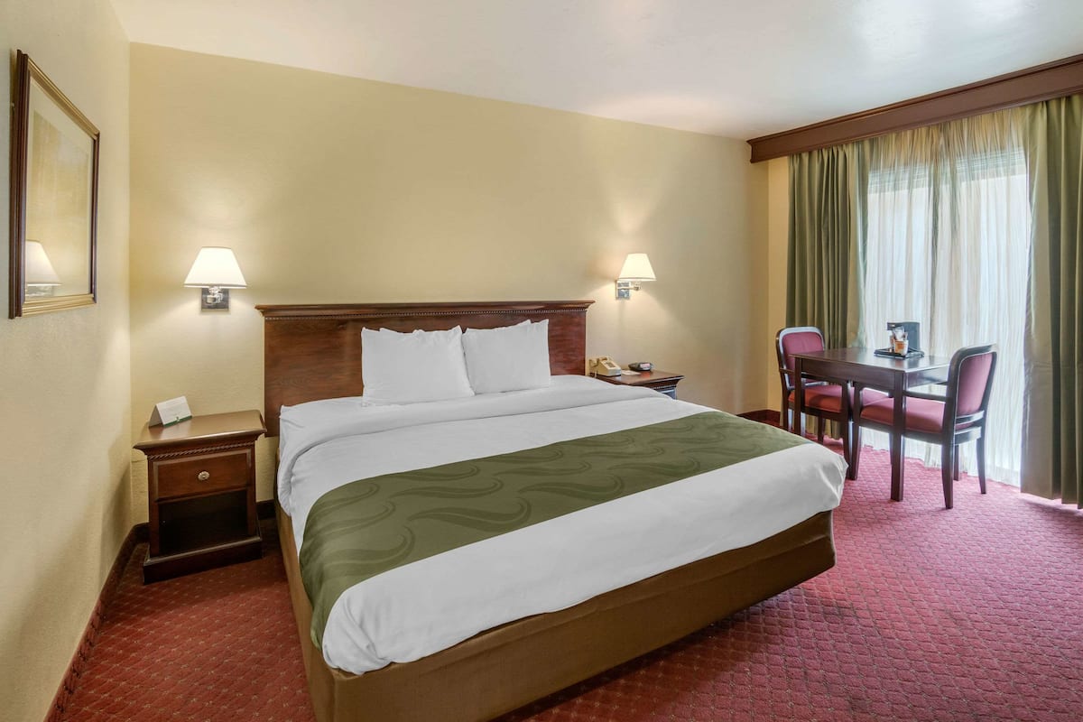 Une chambre d’hôtel avec un grand lit, deux tables de chevet, un bureau avec des chaises et une fenêtre avec des rideaux.