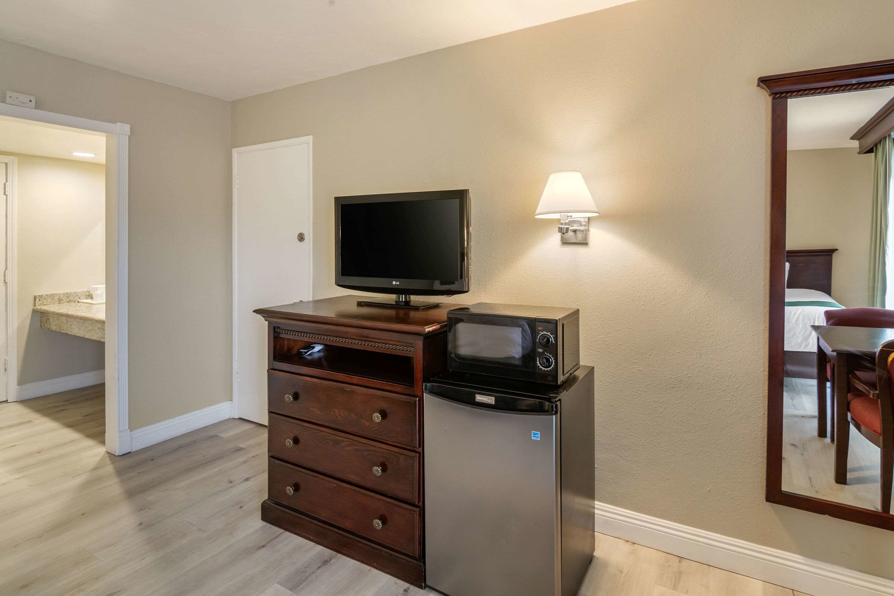 Una kitchenette compacta con microondas, refrigerador y televisor de pantalla plana sobre un mueble de madera.