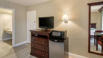 Una kitchenette compacta con microondas, refrigerador y televisor de pantalla plana sobre un mueble de madera.