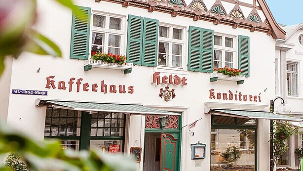 Un bâtiment européen traditionnel abritant un café et une pâtisserie au rez-de-chaussée, caractérisé par une architecture classique et des volets verts.