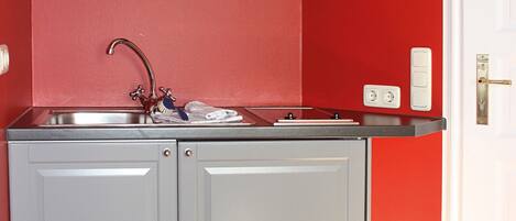 A compact kitchen with a built-in sink, a stainless steel range hood, and a red accent wall.