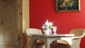 Un coin repas avec des chaises en osier, une table en verre et un tableau représentant des fruits accroché au mur.