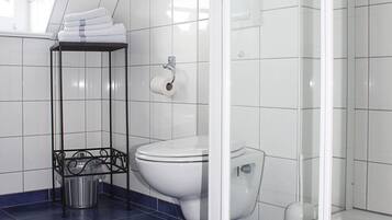 A bathroom with a glass shower enclosure, a toilet, and a metal shelf with towels.