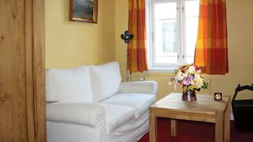 En hvid sofa, et træbord med en vase blomster, og et vindue med gardiner.