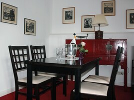 A dining table with four chairs, a wine glass, a vase with a flower, and a red cabinet with framed pictures on the wall.