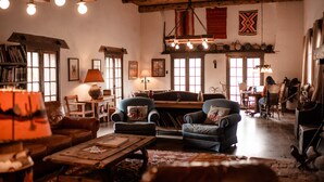 A cozy living room with leather sofas, a wooden coffee table, and a fireplace. There are bookshelves and a dining area in the background. - Kay El Bar Guest Ranch (Wickenburg)