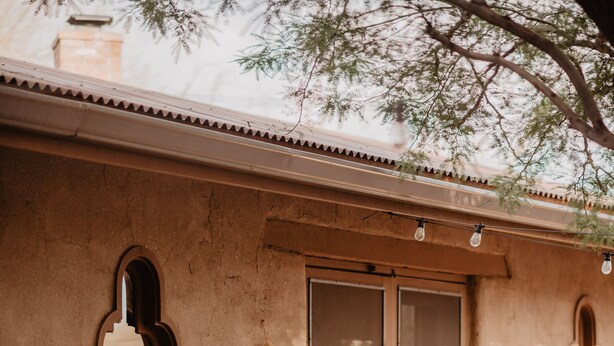 A rustic outdoor area with a stone wall, a wooden stool, terracotta pots with cacti, and a small circular stone feature. - Kay El Bar Guest Ranch (Wickenburg)