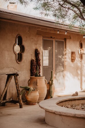 A rustic outdoor area with a stone wall, a wooden stool, terracotta pots with cacti, and a small circular stone feature. - Kay El Bar Guest Ranch (Wickenburg)