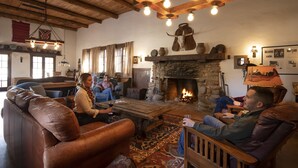 A cozy living room with leather sofas, a stone fireplace, and wooden beams on the ceiling. - Kay El Bar Guest Ranch (Wickenburg)