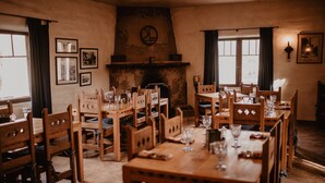 A dining area with wooden tables and chairs, a fireplace, and framed pictures on the walls. - Kay El Bar Guest Ranch (Wickenburg)