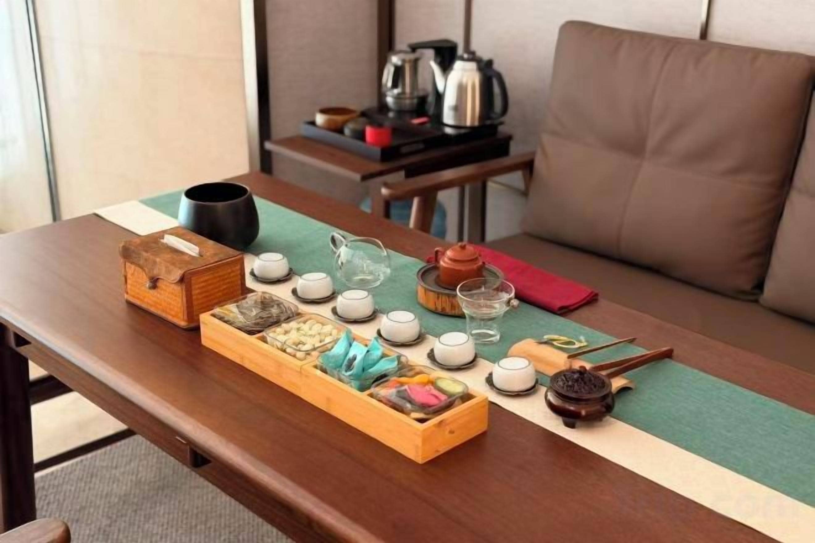 Un juego de té tradicional sobre una mesa de madera con una alfombra verde, una tetera, tazas y una caja de madera con aperitivos.