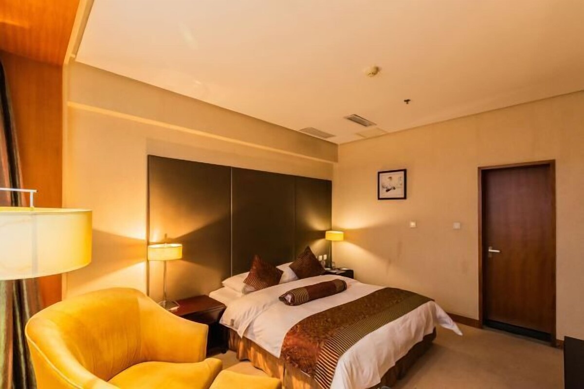 A hotel room with a bed, a chair, a nightstand, and a door.